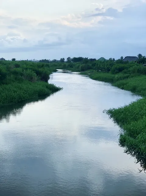A calm creek bordered by green vegetation under a cloudy sky, the Boro Creek waterfront