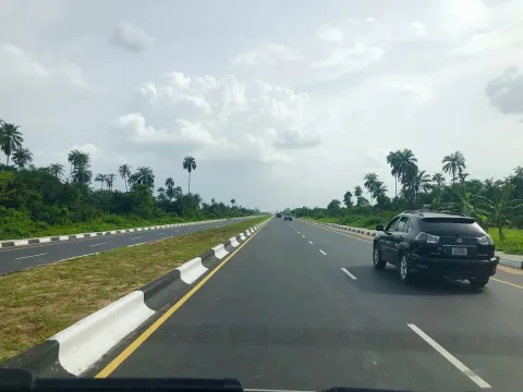 A dual carriageway with a palm-lined green verge and one dark car ahead, described by the photographer as the Igbogene Onopa bypass road