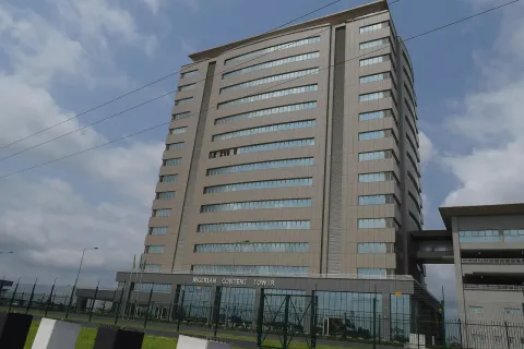 A tall multi-storey office tower with a grey-brown facade seen from ground level under scattered clouds
