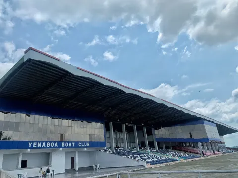 A side view of a long roofed grandstand with blue signage reading Yenagoa Boat Club under a blue sky with clouds