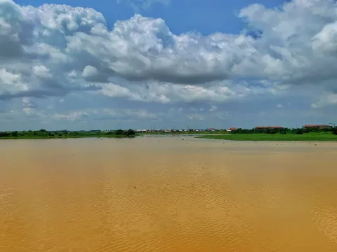 A wide brown river under a large cloudy sky with a low green bank in the distance