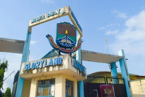 A blue and yellow gatehouse with an arch carrying the words Niger Delta University and the university crest above the sign Gloryland Campus