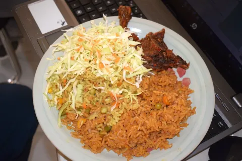 A plate of jollof rice with shredded cabbage salad and a piece of fried fish