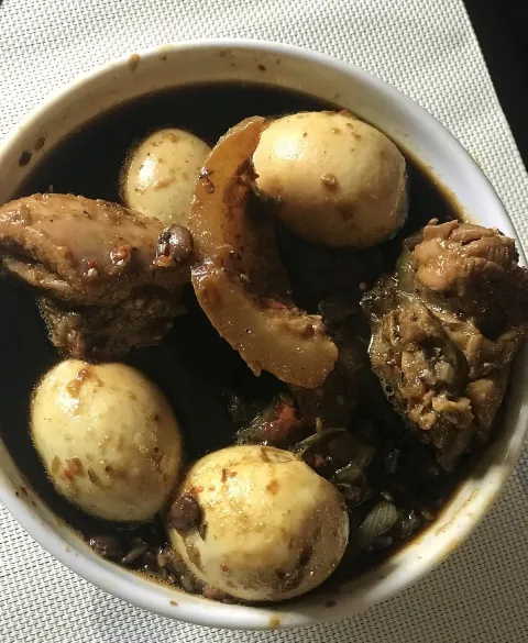 A dark bowl of stew with boiled eggs and pieces of meat, a homemade Nigerian ofada stew