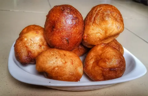Golden-brown puff puff, round fried dough balls, piled on a white dish