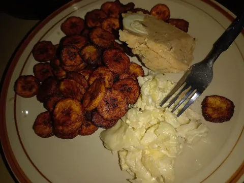Slices of fried plantain with a piece of moi moi and shredded cabbage with mayonnaise on a plate with a fork
